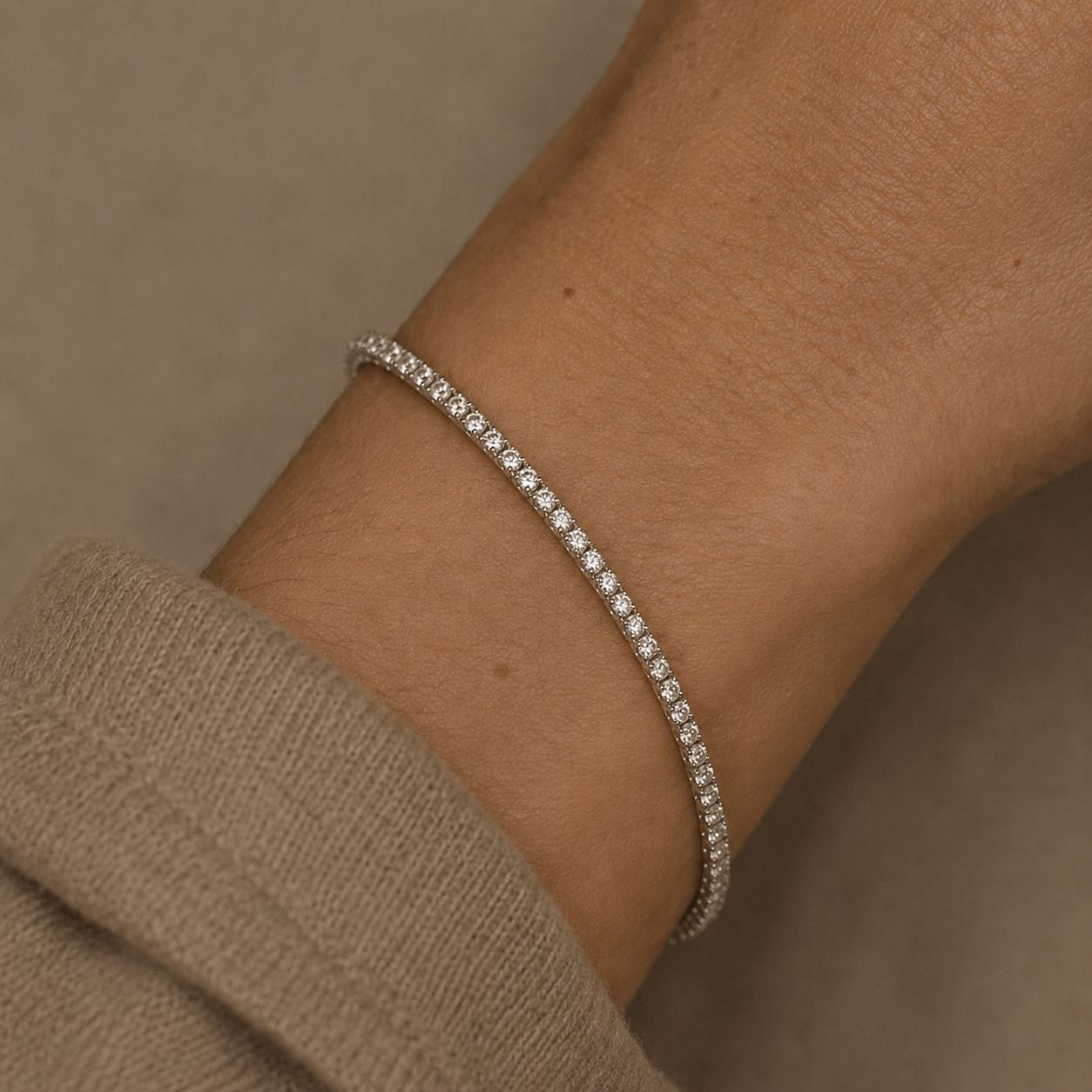 Woman wearing a lab grown diamond tennis bracelet in 14K white gold on a wrist against a neutral background by Camille Jewelry