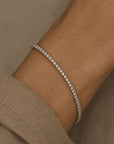 Woman wearing a lab grown diamond tennis bracelet in 14K white gold on a wrist against a neutral background by Camille Jewelry
