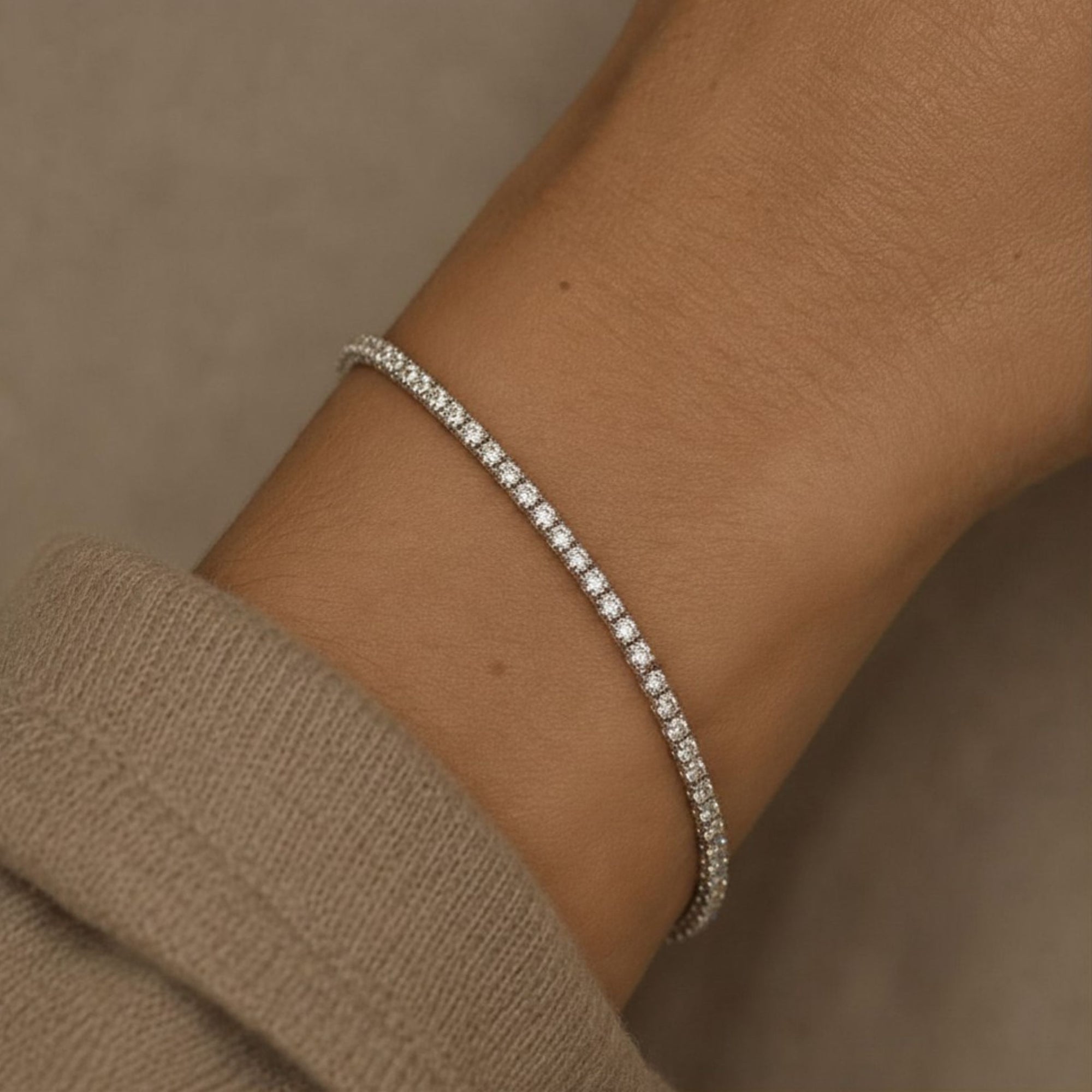 Woman wearing a lab grown diamond tennis bracelet in 14K white gold on a wrist against a neutral background by Camille Jewelry