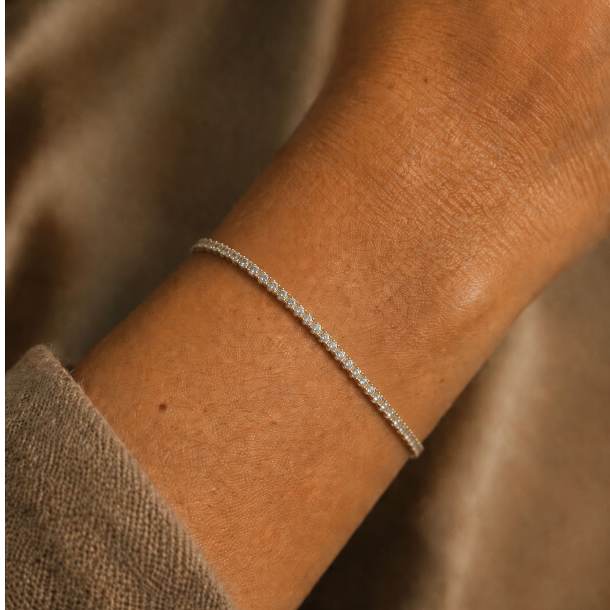 Woman wearing a lab grown diamond tennis bracelet in 14K white gold on a wrist against a neutral background by Camille Jewelry