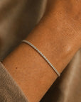 Woman wearing a lab grown diamond tennis bracelet in 14K white gold on a wrist against a neutral background by Camille Jewelry