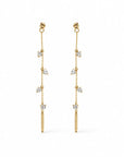 A pair of gold dangle linear earrings with trillion shaped cubic zirconia stones, displayed against a solid white background by Camille Jewelry