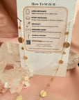 Gold plated disc charm convertible necklace and eyeglass chain on card with description of how to wear it displayed on a quartz stone and pink background by Camille Jewelry. 