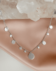 Silver plated disc charm convertible necklace and eyeglass chain displayed on a quartz stone and soft pink background by Camille Jewelry.