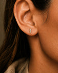 Mini diamond bar stud earrings in 14K yellow gold on models face close up by Camille Jewelry.