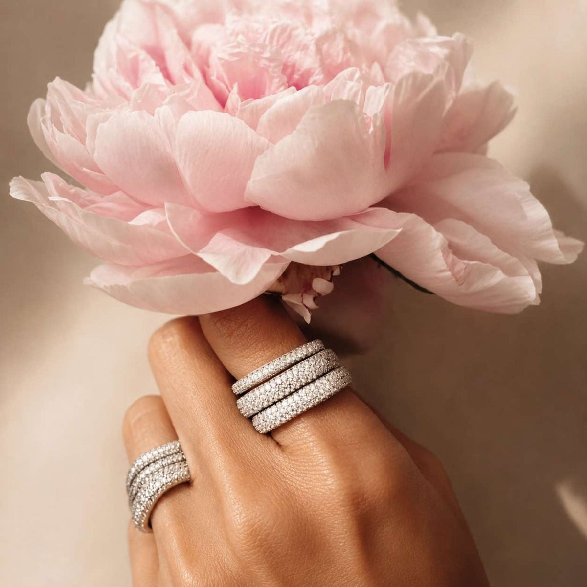 Hand wearing two pave sterling silver square rings with a pink flower in the background, by Camille Jewelry. 