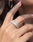 A close-up of a woman's hand wearing a stack of two gold plated sterling silver square pave rings, with pink manicured nails and a silver hoop earring visible, by Camille Jewelry. 