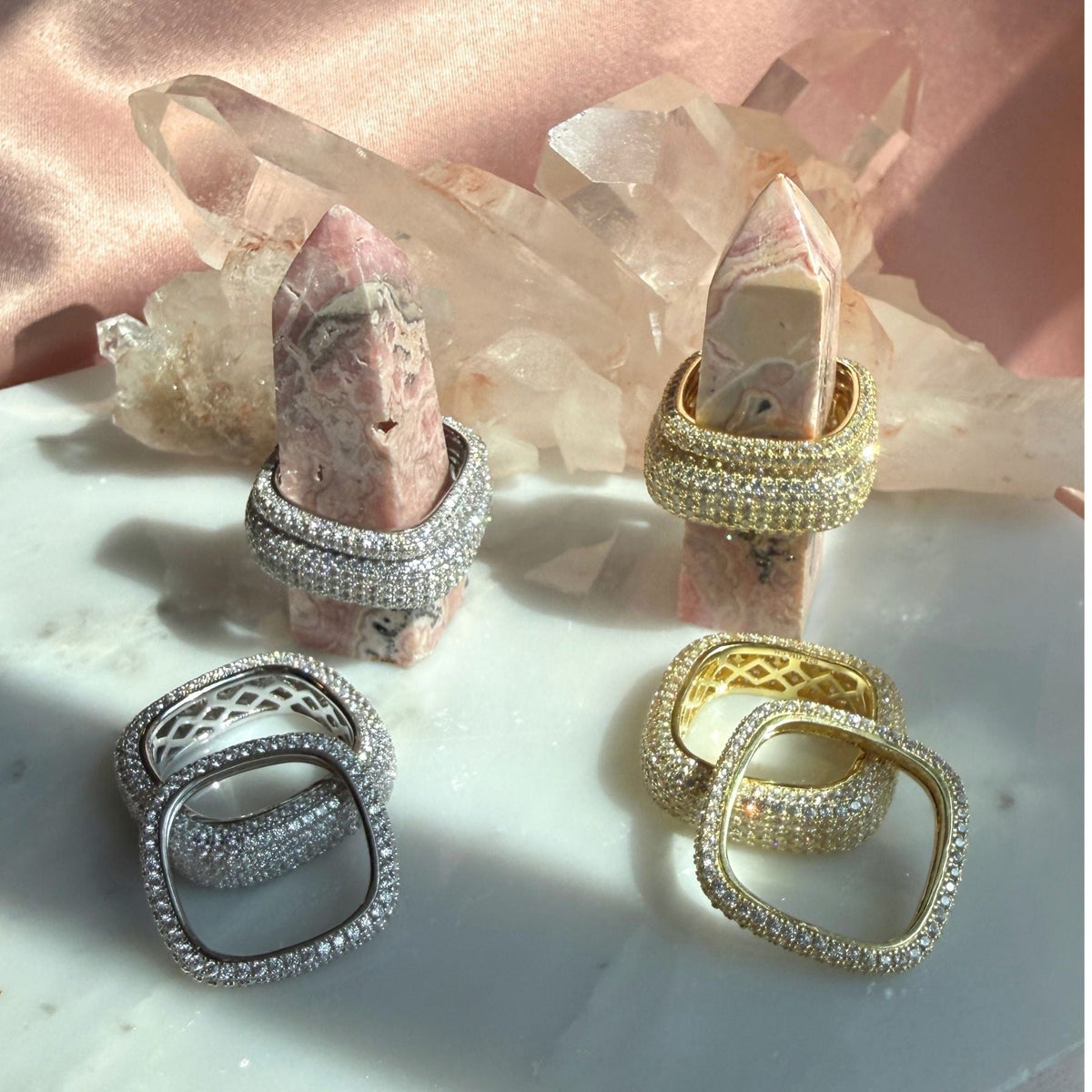 Skinny and wide square rings displayed on crystal points against a pink satin backdrop. Featuring rhodium plated silver  and gold plated silver with pavé-set clear stones by Camille Jewelry. 
