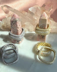 Skinny and wide square rings displayed on crystal points against a pink satin backdrop. Featuring rhodium plated silver  and gold plated silver with pavé-set clear stones by Camille Jewelry. 