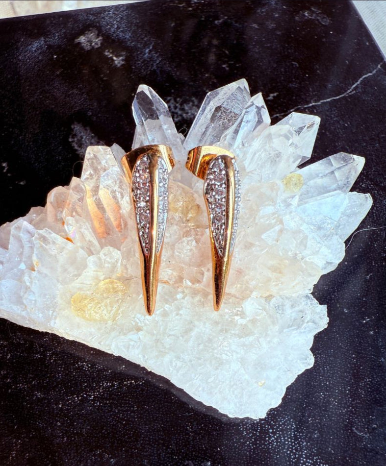 Gold bird beak stud earrings on a crystal with 'Camille Jewelry' branding Phoenix Collection.