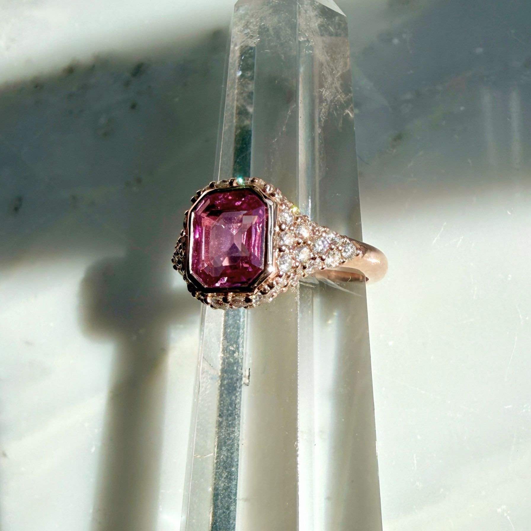 A pink sapphire ring in natural diamonds set in 14k rose gold on a quartz display by Camille Jewelry
