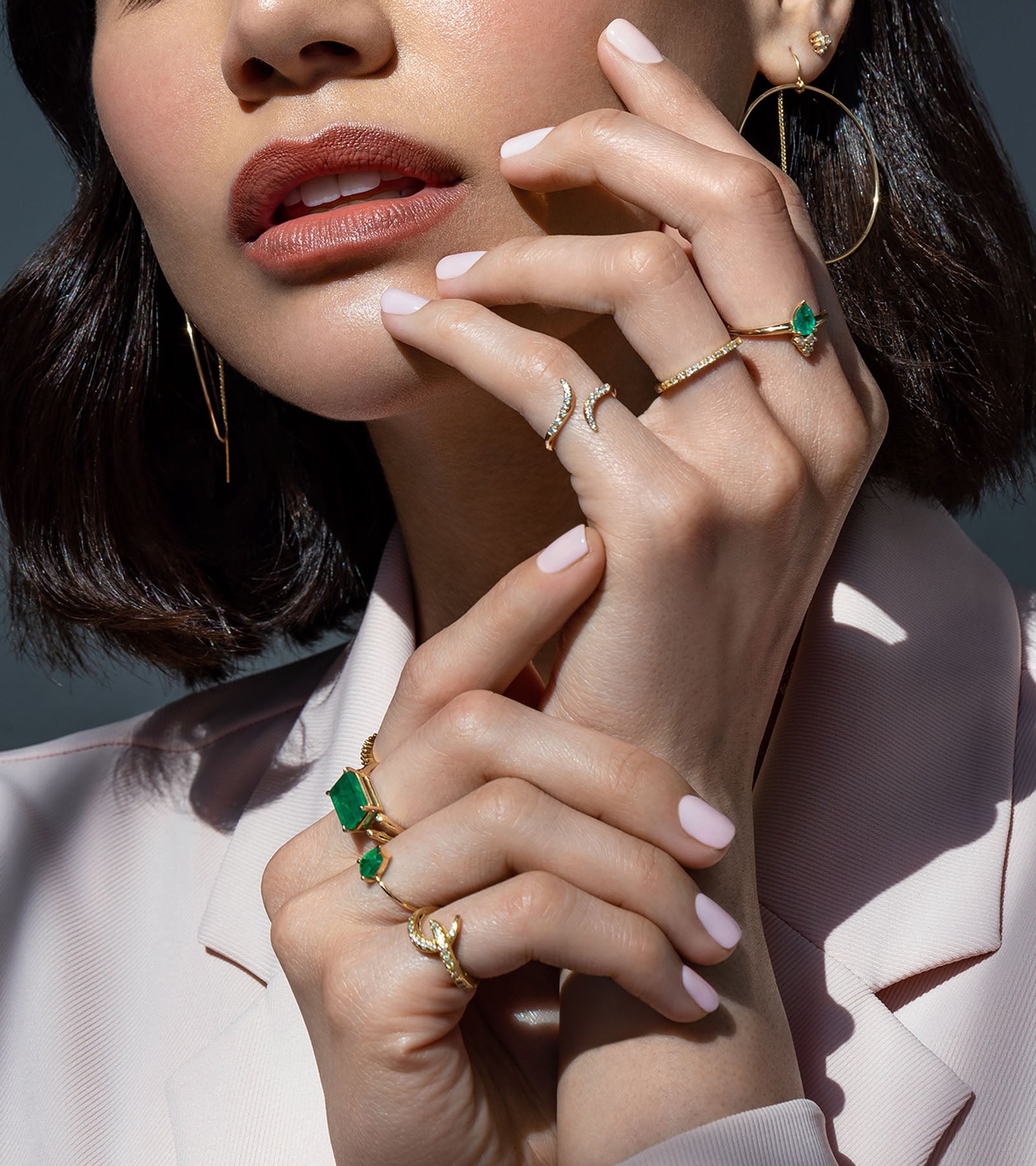 model wearing emerald and diamond rings and wearing a light pink jacket in Camille Jewelry. 