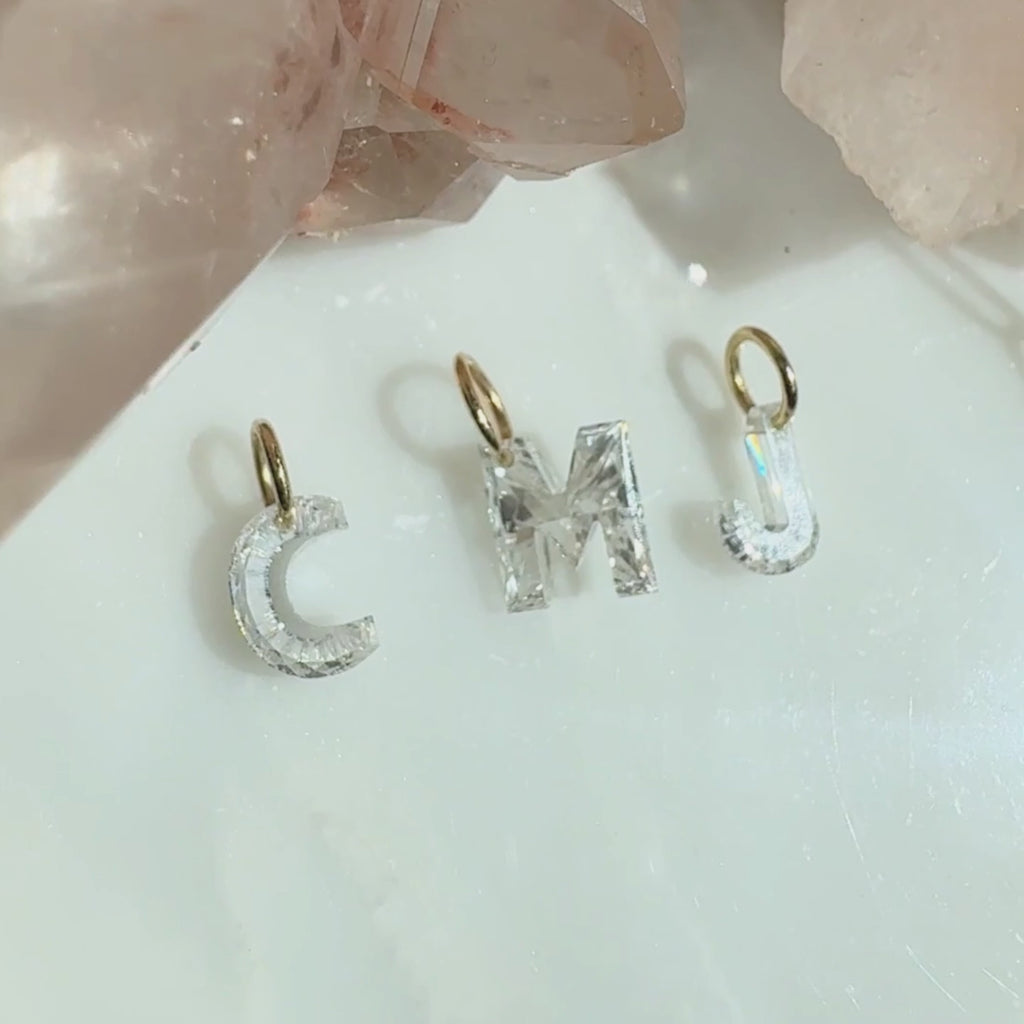 Floating lab created diamond initials in "CMJ" suspended from 14K yellow gold jump rings laying on a quartz stone display , by Camille Jewelry