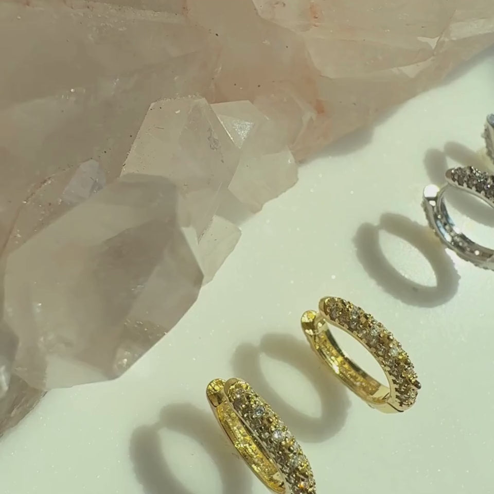 Video of gold and sterling silver studded pave huggie earrings on a soft white display by Camille Jewelry. 