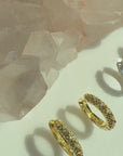 Video of gold and sterling silver studded pave huggie earrings on a soft white display by Camille Jewelry. 