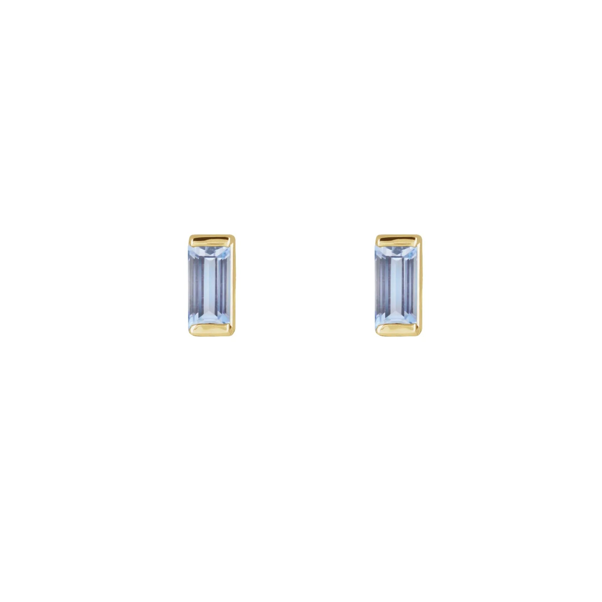 Pair of tiny stud earrings in tanzanite in 14k yellow gold on a white background by Camille Jewelry. 