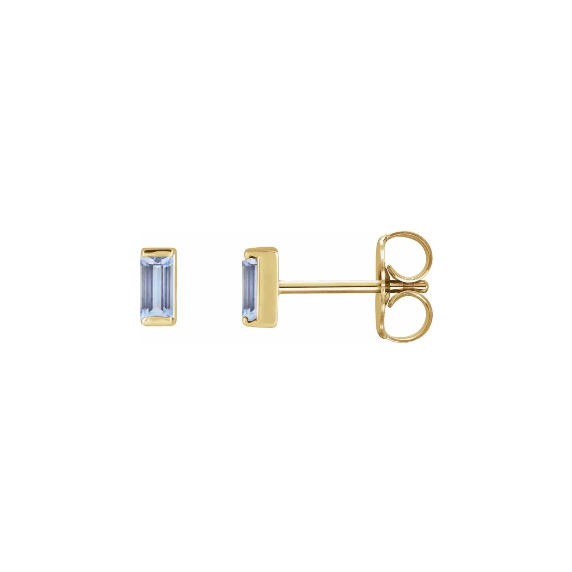 Tiny stud earrings in tanzanite gemstone set in 14k yellow gold on white background by Camille Jewelry. 